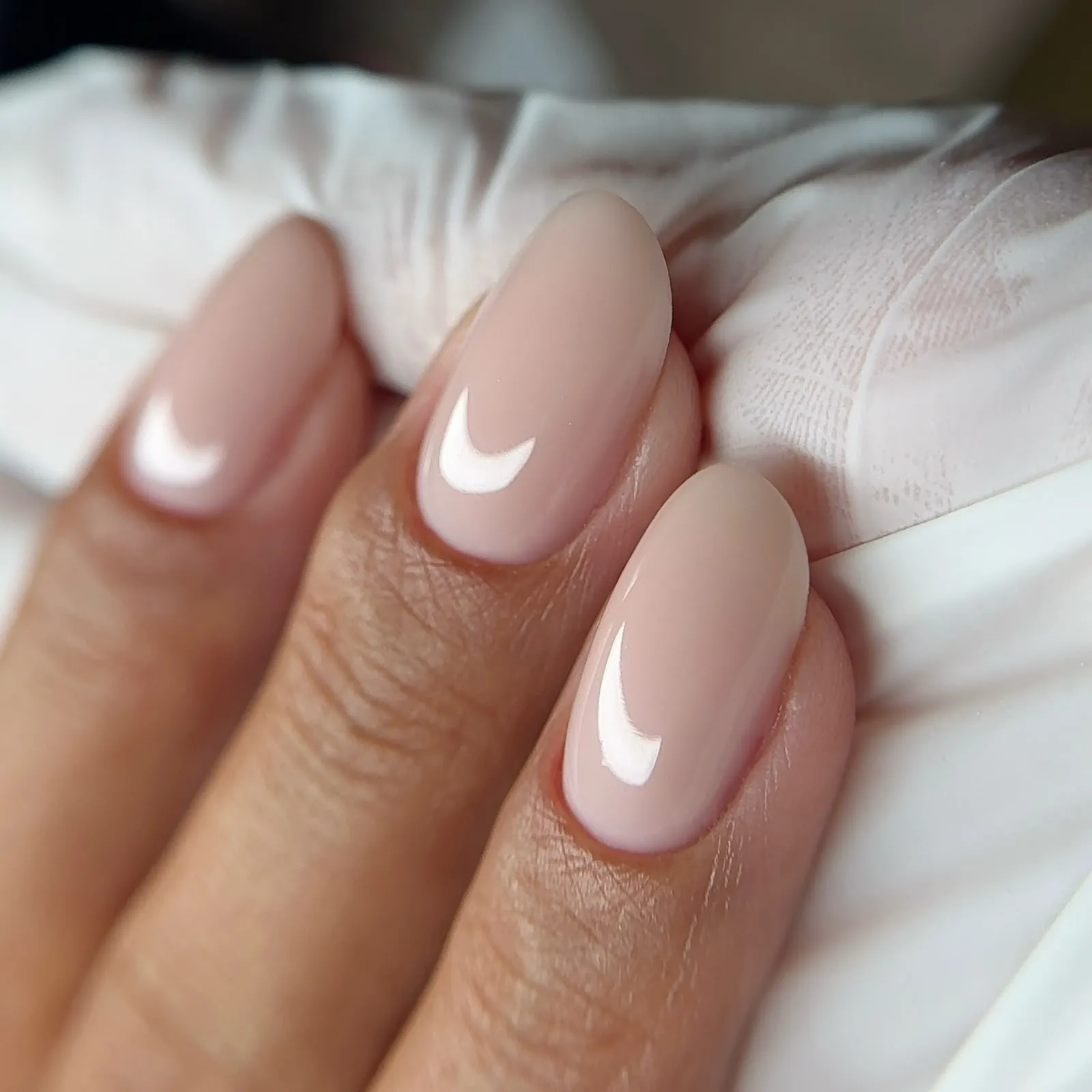Gros plan sur des ongles amande nude, très brillants, posés sur un linge blanc.