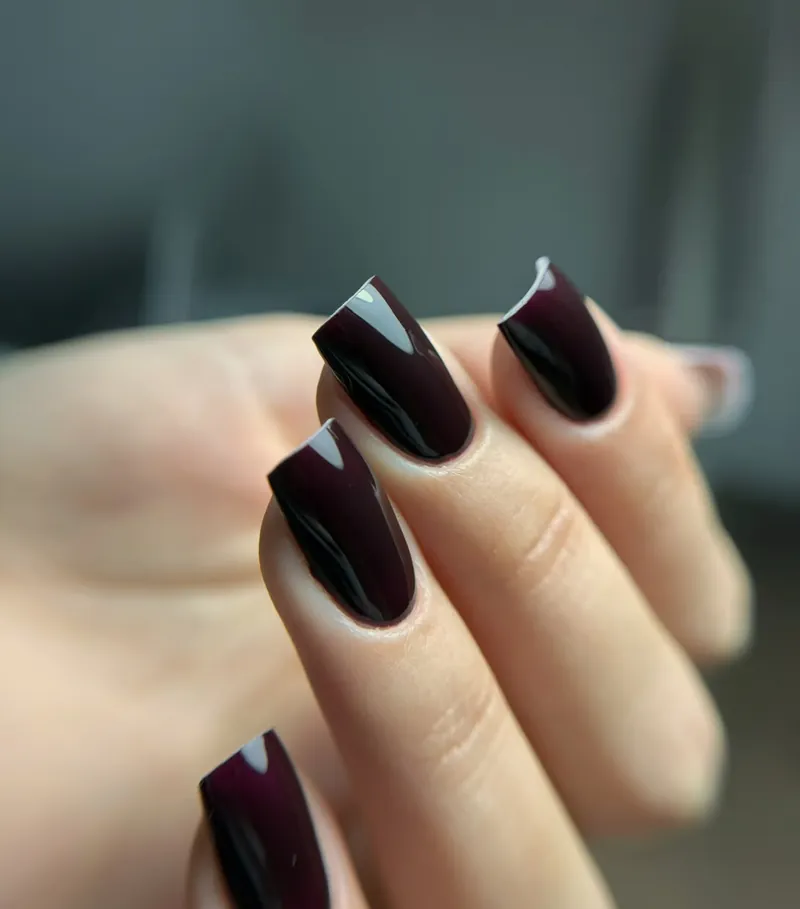 Ongles carrés laqués bordeaux sur une main fine.